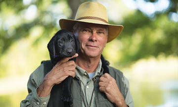 Man in hat carrying black puppy