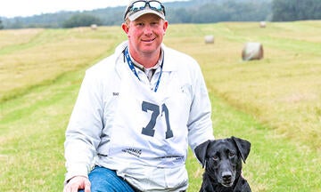 Ray Voigt kneeling with his black lab beside him