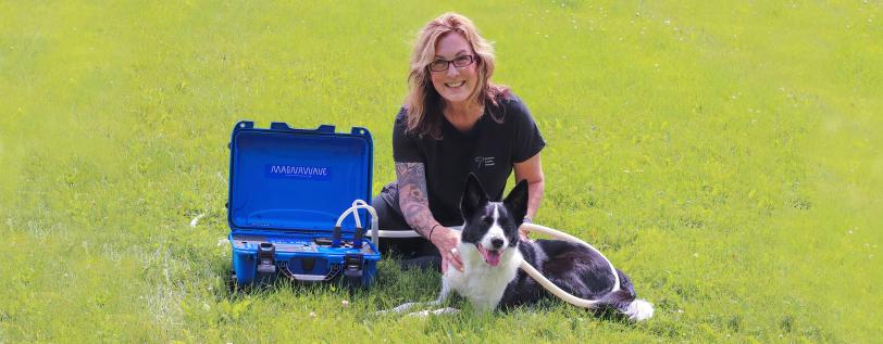 Madison Canine Massage owner posing with massage kit and dog in field.