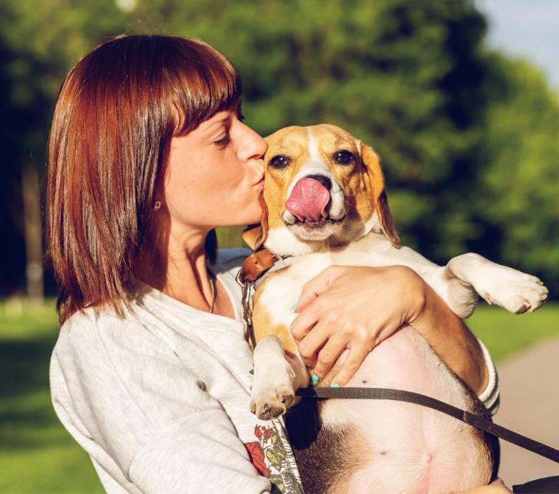 A dog owner holding and kissing their dog while on a walk at a park.