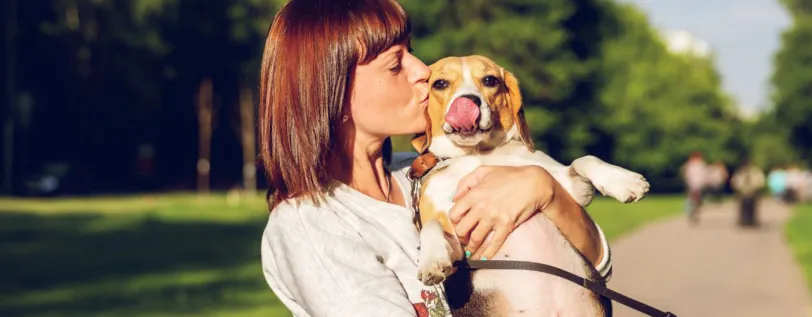 A dog owner holding and kissing their dog while on a walk at a park.     