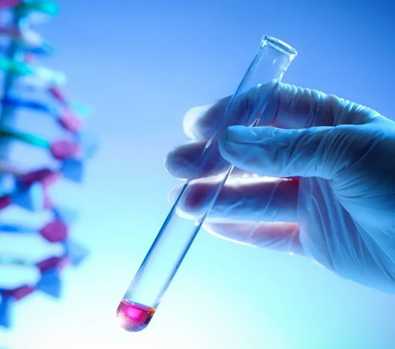 A gloved hand holding a vial with pink liquid at the bottom and a DNA strand model in the background.