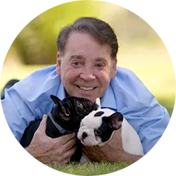 Perry Payson laying in the grass with two French Bulldog puppies.