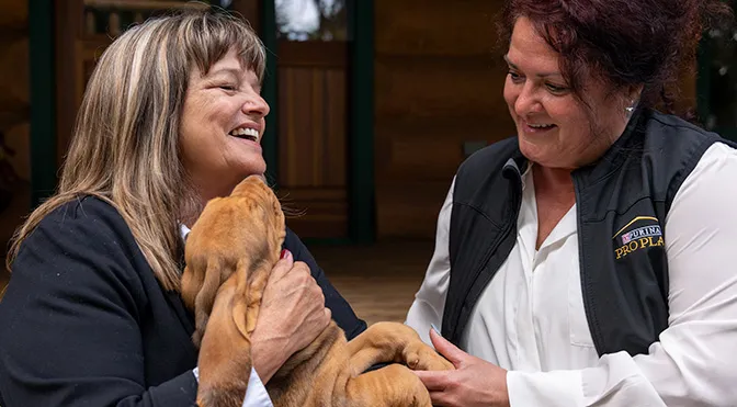 Two smiling women sitting next to each other holding a puppy.