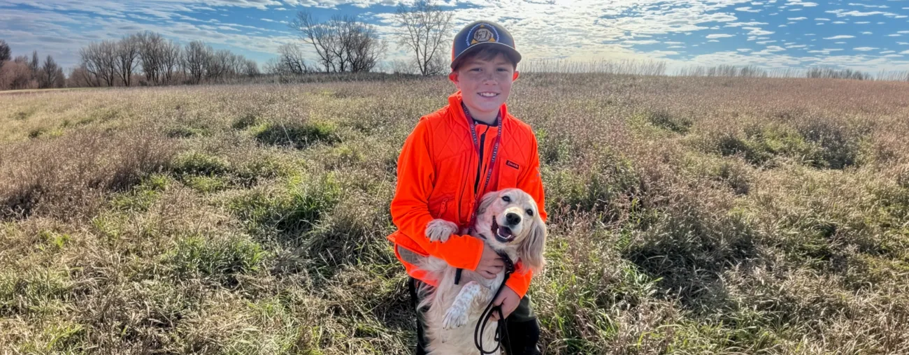Handler, Eli Simms, holds cocker spaniel, Lila, in a grassy field.