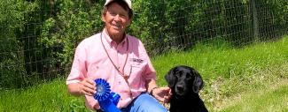 Bob West posing with medal and black lab in a field. 