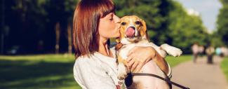A dog owner holding and kissing their dog while on a walk at a park.     